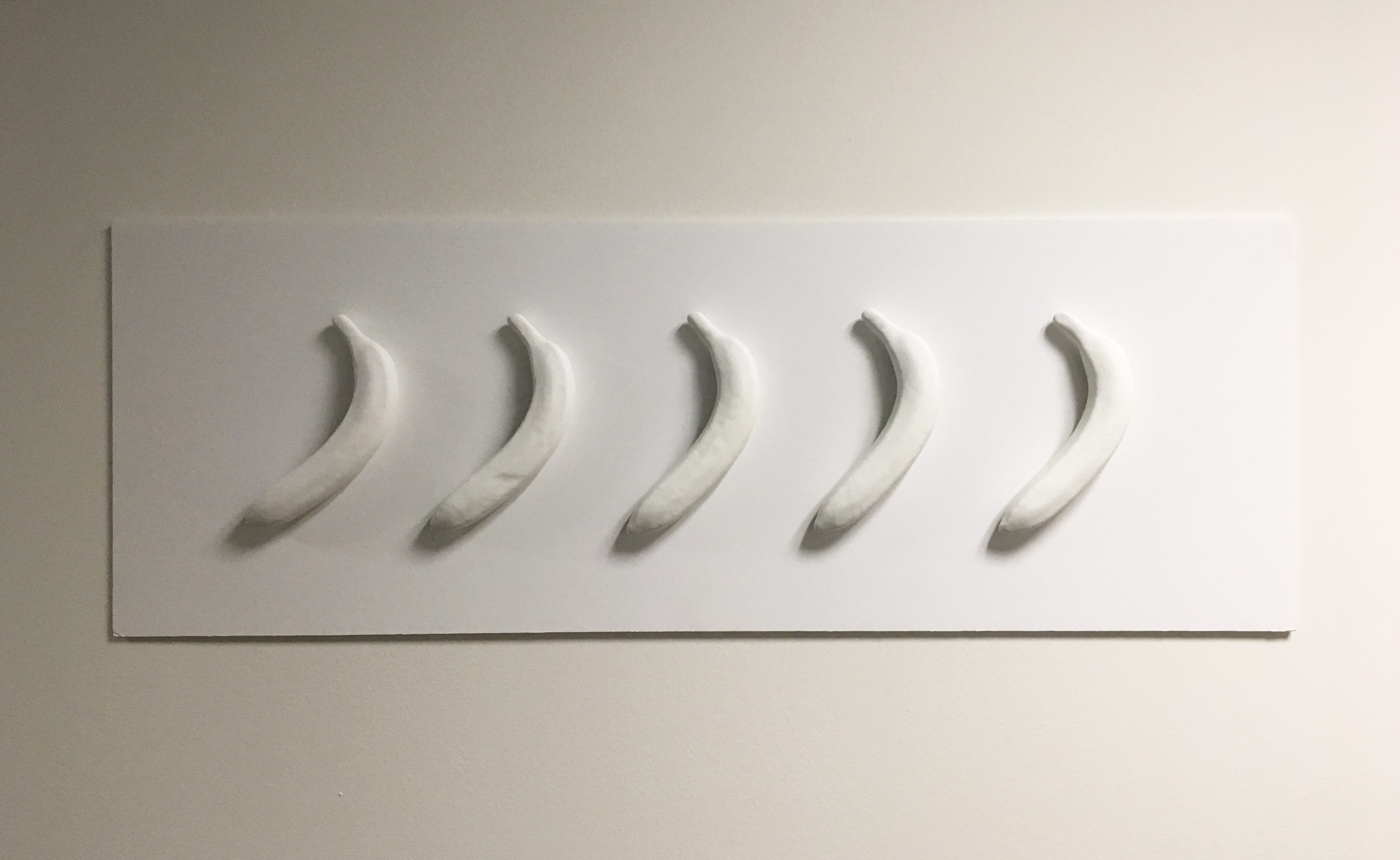 Five plastic bananas painted in white and pasted to a white wall.